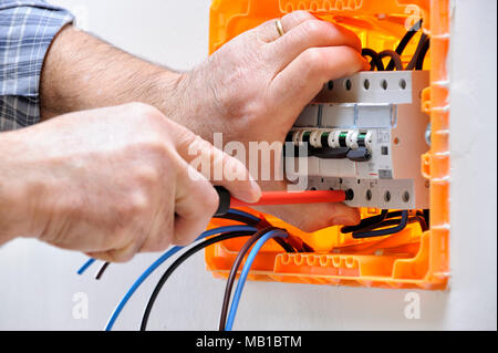 Electrician technician working on a residential electrical panel, fixing with a screwdriver the cable in the magnetothermal switch Stock Photo