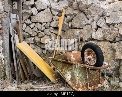 Old rusty wheelbarrow lying on the floor in front of stone wall in Lubenice, Cres Croatia Stock Photo