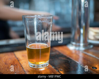 Almost empty pint glass of beer sitting on wooden bar for last call Stock Photo