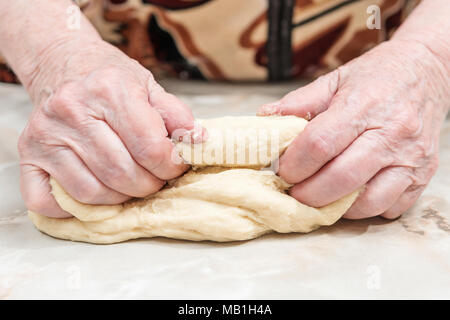 Hands of an elderly woman knead the dough on a table, close-up Stock Photo