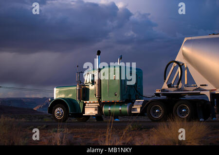 Big rig classic green semi truck with capacity compartment behind of tractor cab transporting bulk semi trailer carries cargo on the Arizona road in t Stock Photo