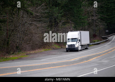 Big rig white bonnet semi truck with reefer semi trailer stand out of winding curved road on the sideline in green forest in Columbia Gorge national r Stock Photo