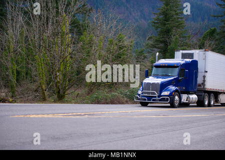 Dark blue American bonnet day cab big rig semi truck with grille guard for local deliveries carry refrigeration semi truck transporting goods on wide  Stock Photo