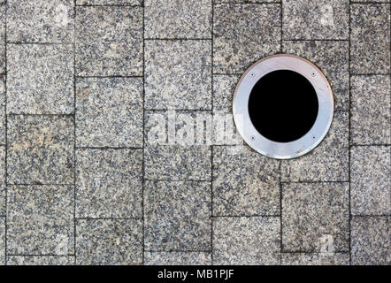 The city pavement is lined with square marble tiles. Round lamp is mounted on the surface of the street. Stock Photo