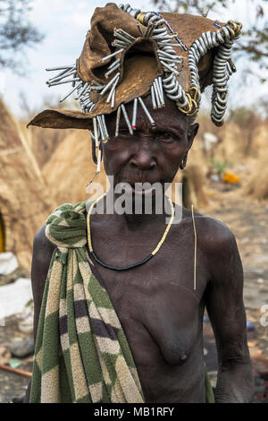 OMORATE, ETHIOPIA - JANUARY 24, 2018: Woman of the Mursi tribe with traditional jewelry with the typical houses of the Mursi in Ethiopia. Stock Photo