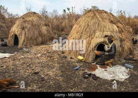 Omorate, Ethiopia - January 24, 2018: Woman of the Mursi tribe drinking in a bowl next to her house in a traditional village of the Mursi in Ethiopia. Stock Photo