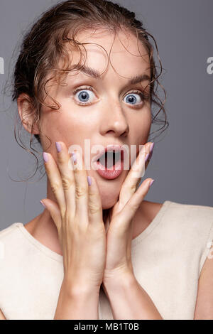 Amazed young woman with hands near face and mouth open. Shocked girl with bulging eyes. Surprised female screaming with expressive facial expressions Stock Photo
