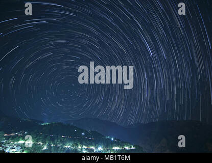 McLeod Ganj at night with star trails in sky above mountains, India Stock Photo