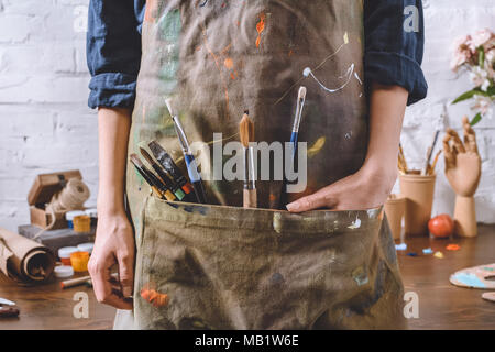 cropped image of artist with brushes and hand in apron pocket Stock Photo