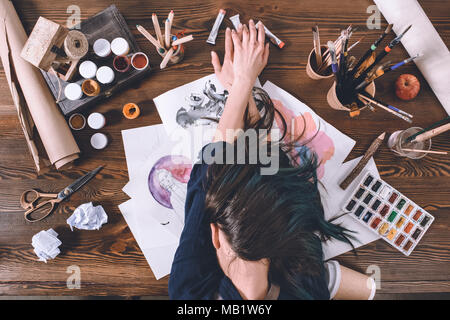 top view of female artist sleeping on sketches and paints at workplace  Stock Photo