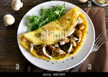 Omelet stuffed with mushrooms, pieces of chicken meat, greens on wooden table. Close up view Stock Photo