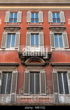 Looking up at the walls and windows of an old apartment building in Rome, Italy. Deep red in colour, weathered with the patina of city life. Stock Photo