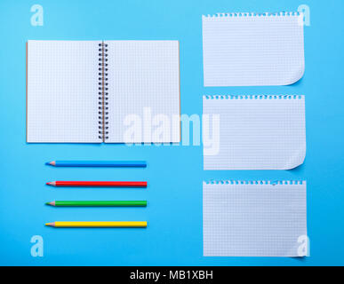 white blank sheet in a box from a notebook with holes and multi-colored wooden pencils on a blue background Stock Photo