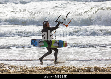 Sandbanks, Poole, Dorset, UK. 6th April, 2018. UK weather: breezy day at Sandbanks as kite surfers make the most of the windy conditions. Kitesurfer carrying kite board heading into the sea. kitesurfers kite surfers kite surfer kiteboarders kite boarders kitesurfer kitesurfing kite surfing kiteboarding kite boarding kiteboarder kite boarder Stock Photo