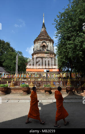 two young monks walking by in front of the big pagoda Chedi of temple Wat Lok Mori, Chiang Mai, Thailand Stock Photo