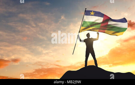 Central African Republic flag being waved by a man celebrating success at the top of a mountain. 3D Rendering Stock Photo