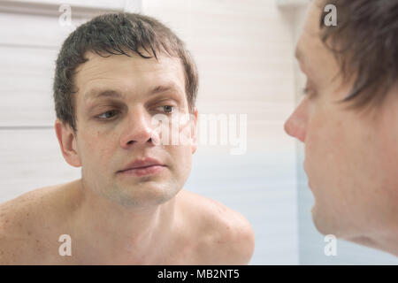 A clean-shaven young man looks in the mirror Stock Photo