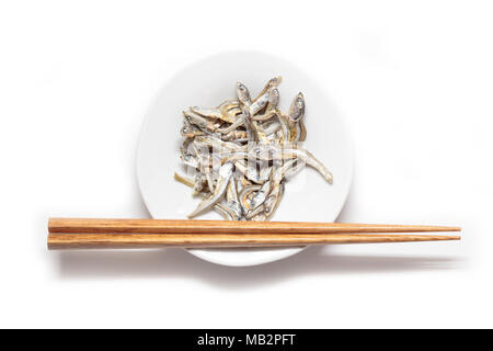 Japanese dried infant sardine with wooden chopsticks isolated on white backgroung. Japanese cuisine. Healthy snack food. Niboshi or Iriko fish. Stock Photo