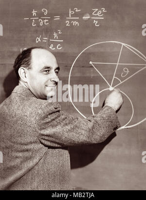 Enrico Fermi (1901–1954), Italian-American physicist and pioneer in nuclear fission, demonstates a physics equation on a chalkboard, c1950. Fermi worked on the Manhattan Project during World War II and made significant contributions to the development of quantum theory, nuclear and particle physics, and statistical mechanics. Stock Photo