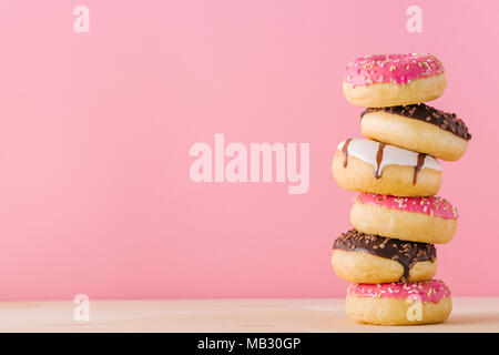 Stack of tasty sweet different colored donuts on a table on pink background. Stock Photo