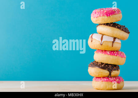 Stack of fresh tasty different colored donuts on the blue background. Stock Photo