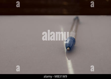 The blue ballpoint pen of simple design lies on a sheet of white paper with a ray of sunlight. Stock Photo