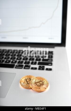 Two golden bitcoins as main cryptocurrencies placed on silver laptop with blurred chart on screen on background. Digital virtual money electronic currency blockchain future trend innovative banking Stock Photo