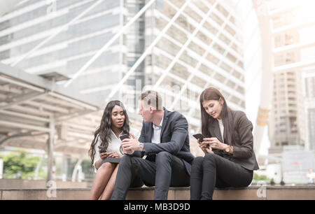 Group of young people use their phones in city talking and smiling Stock Photo