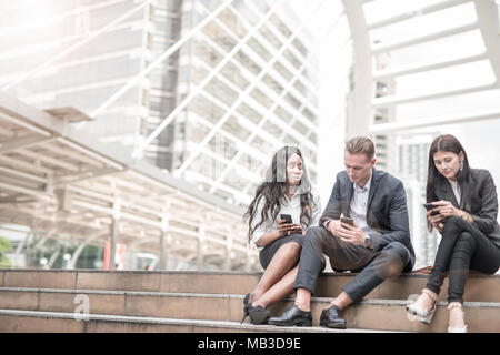 Group of young people use their phones in city talking and smiling Stock Photo