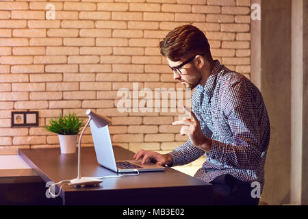 A man bearded freelancer with a laptop works in the evening. Stock Photo