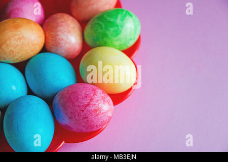 bright colorful Easter eggs on red plate on pink background. Stock Photo
