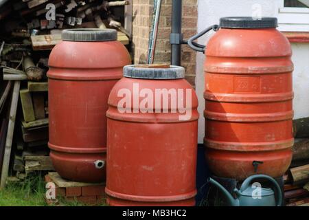 Three red water butts and green watering can in a garden