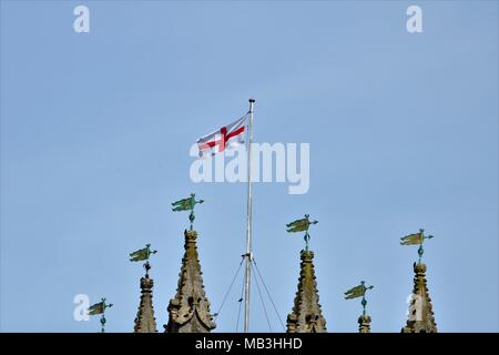 St George's flag flying in the wind on top of a church next to spirals / towers against a clear blue sky Stock Photo