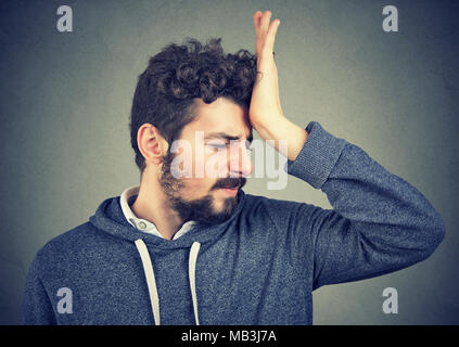 Regrets wrong doing. Portrait silly young man, slapping hand on head having a duh moment isolated on gray background. Negative emotion expression feel Stock Photo