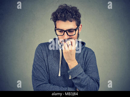 Closeup portrait nervous man biting fingernails craving something and anxious on gray wall background. Negative human emotion facial expression percep Stock Photo