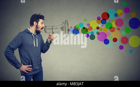 Portrait young man holding screaming in megaphone isolated on gray background. Propaganda, breaking news, social media communication concept Stock Photo