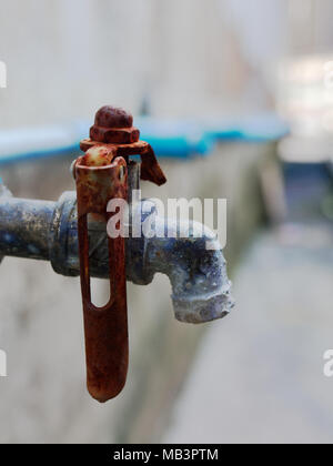 Old rustic faucet from blue plastic pipe with red handle and brass spout over cement wall background in retro or vintage style Stock Photo