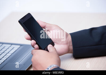 young business man using smart phone, business concept, hand holding phone and touching on home button and black screen of phone with part of laptop Stock Photo