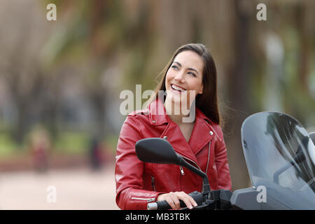 Biker thinking looking at side on her motorbike on the street Stock Photo