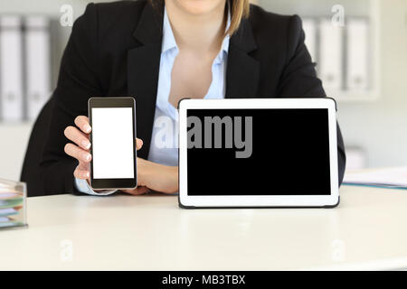 Front view close up of a businesswoman showing blank tablet and phone screens on a desktop at office Stock Photo