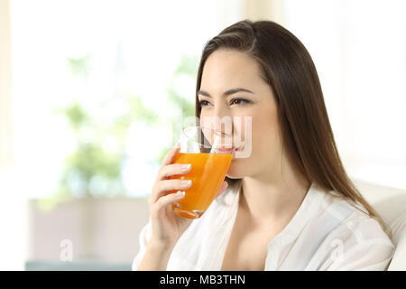 Woman drinking orange juice in a glass sitting on a couch in the living room at home Stock Photo