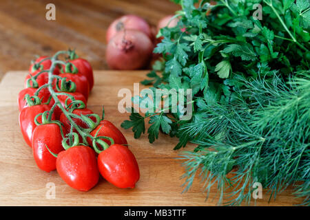 Grape tomatoes on vine  on wood chopping board next to a bunch of fresh dill and parsley. Stock Photo