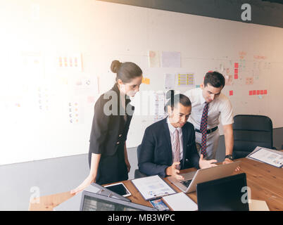 Serious business people showing team work while working in board room in office interior. People helping one of their colleague to finish new business Stock Photo
