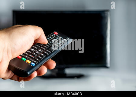 hand holding a remote control and behind a tv on white background Stock Photo