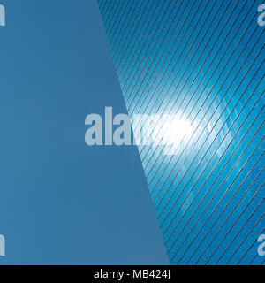 Blue background. The left side is blue sky, the right half is a modern blue glass office building with a spot that is reflection of the sun Stock Photo
