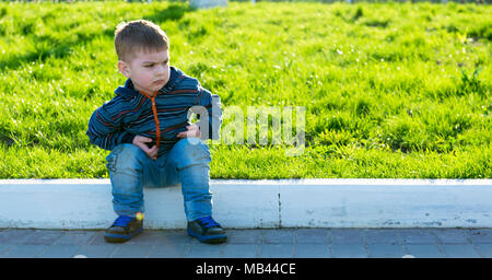 Serious capricious boy is sitting on the road Stock Photo