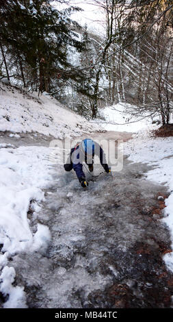 male ice climber free solo climbing a narrow frozen and steep creek in the winter forest Stock Photo
