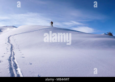 a backcountry skier hiking up on a long mountain ridge towards the summit near Klosters in the Swiss Alps in deep winter Stock Photo