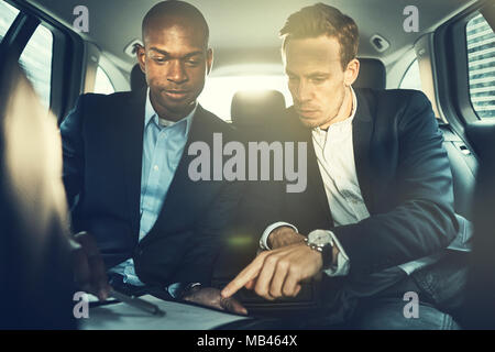 Two diverse businessmen discussing paperwork while sitting in the backseat of a car driving through the city Stock Photo
