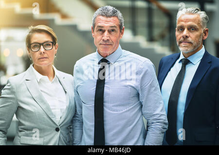Focused mature businessman standing confidently with two colleagues in the lobby of a modern office building Stock Photo